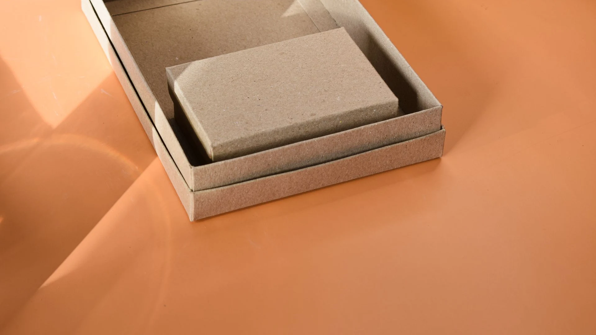 Plain unbranded kraft packaging boxes nested together on an orange surface