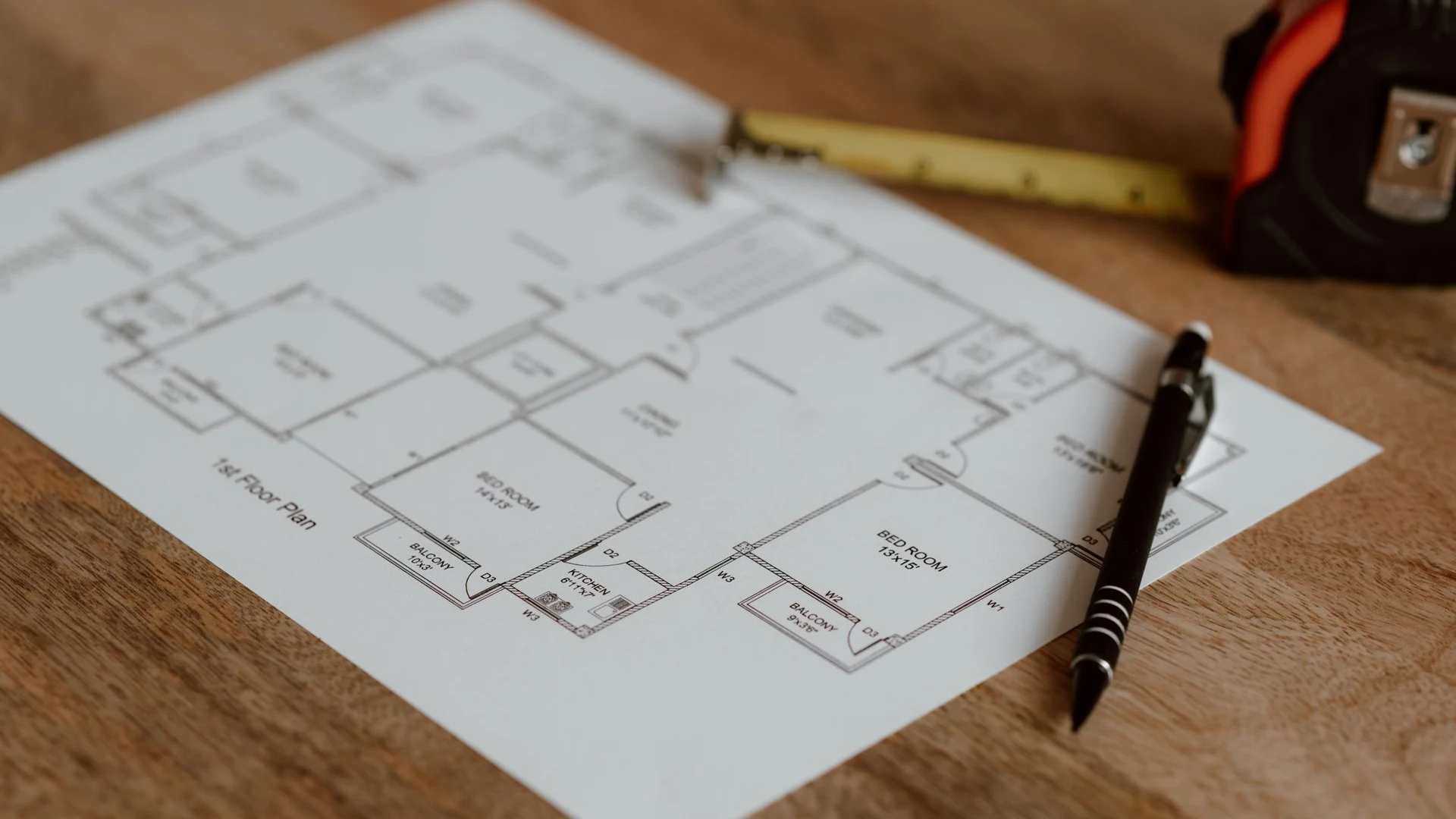 Architectural floor plan laid out on a wooden desk with a tape measure and pen