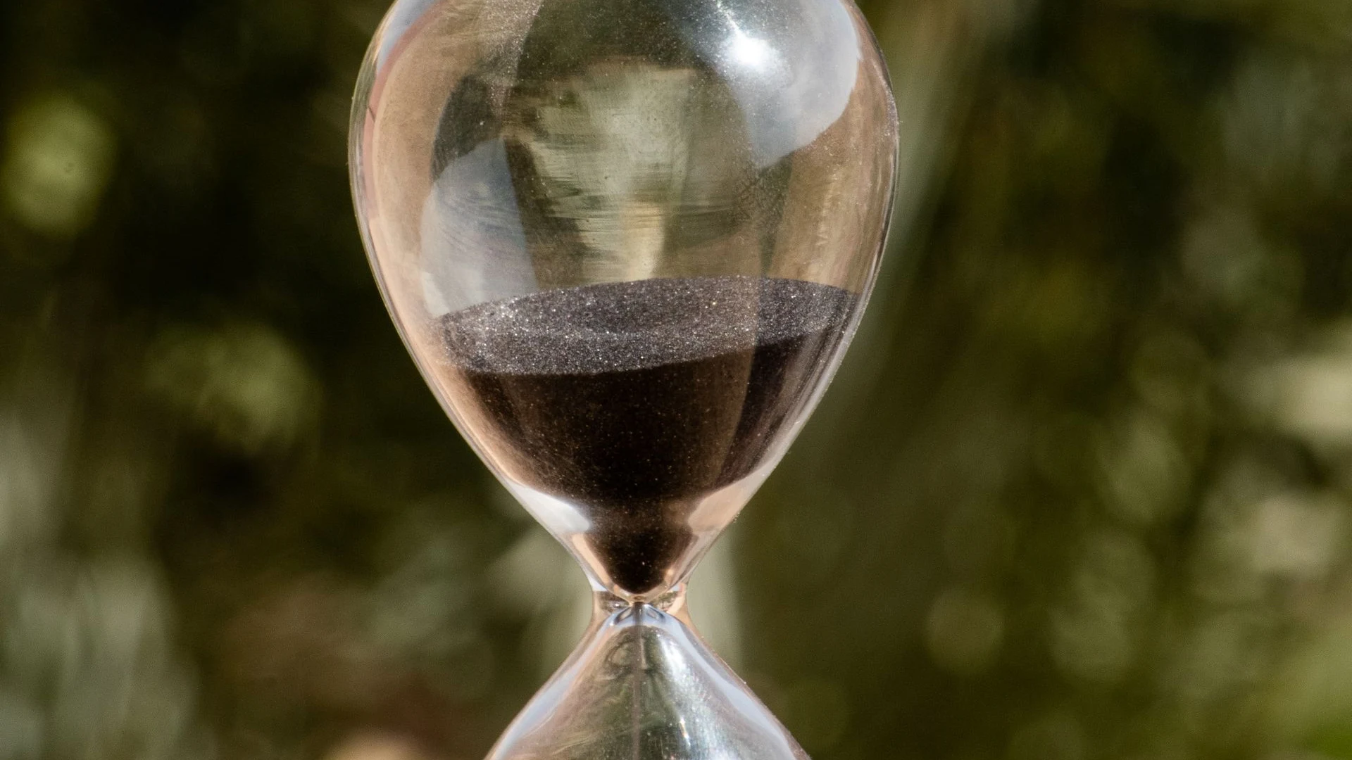 Glass hourglass with dark sand outdoors