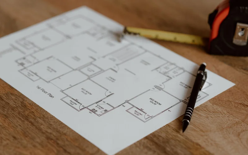 Architectural floor plan laid out on a wooden desk with a tape measure and pen