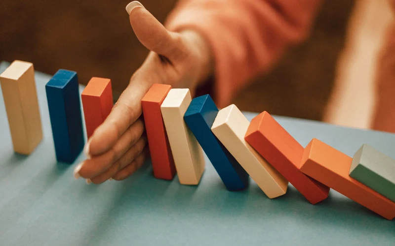 Hand stopping a falling row of colourful dominoes